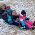 A women and three children sitting on a sled on the snow covered ground.