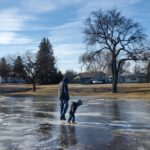 A man and child standing on an outdoor ice skating rink.