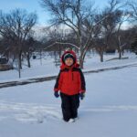 A child standing outside in a park with snow on the ground.