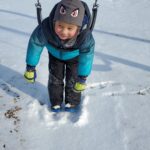 A child hanging on a swing outdoors during the winter.