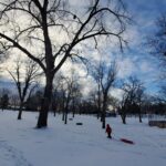 A child outdoors in a park pulling a slide on the snow.