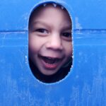 A child sticking his head through a hole in a piece of playground equipment.