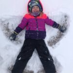 A child creating a snow angel on the ground.