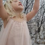 A child with a pink dress standing outside in the snow.