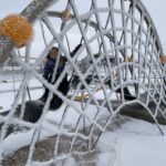 A child on a piece of playground equipment covered in frost.