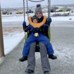 A women and child on a swing outdoors during the winter.