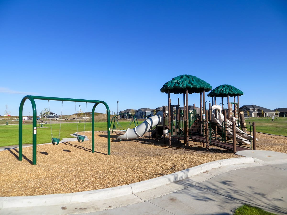 green, brown, and white playground with a swing set at Heritage Park