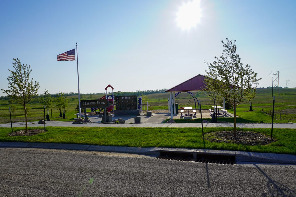 Heroes Park featuring a picnic shelter, playground, and heroes plaza with an American flag on a flag pole