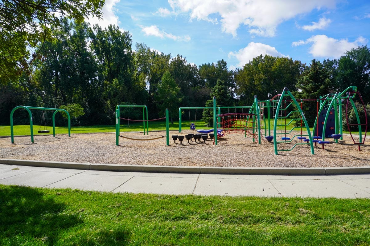 green and red playground at Jaycee Centennial Park with tall trees in the background and a cloudy sky