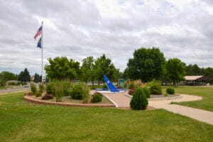 sundial, plants, and flags on a flag pole at Optimist Family Park, shelter in the background