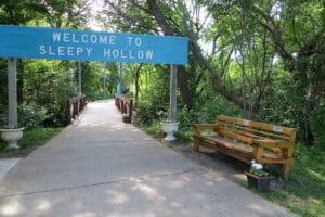 welcome sign to Sleepy Hollow Park with a park bench next to the trail