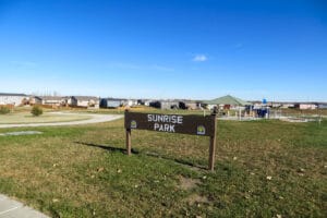 park sign at Sunrise Park with playground and shelter in the background