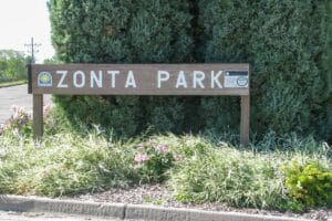 Zonta Park brown sign at park entrance with plants surrounding it