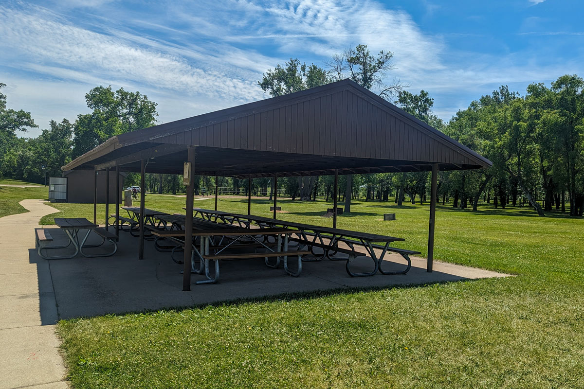outdoor shelter with picnic tables with trees and a sand volleyball court in the background