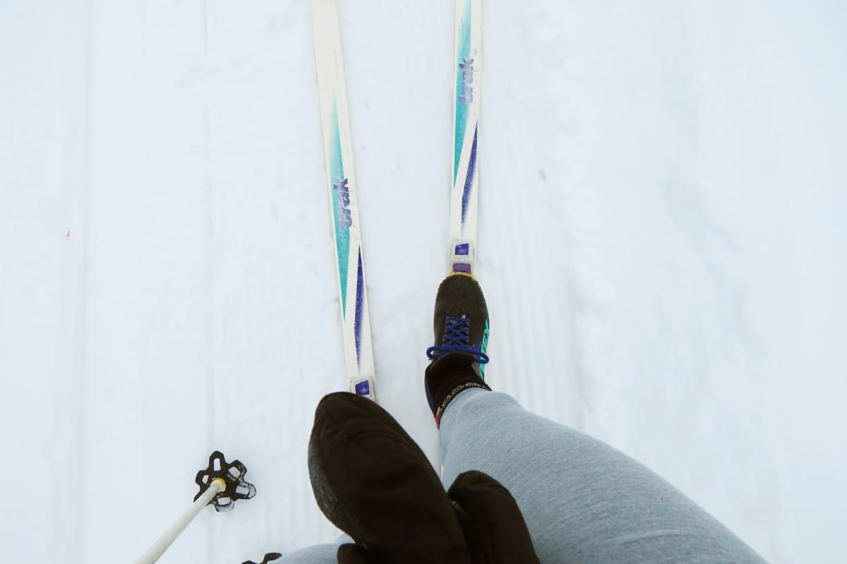 Cross-country skier looking down at feet in skis and pole on ground