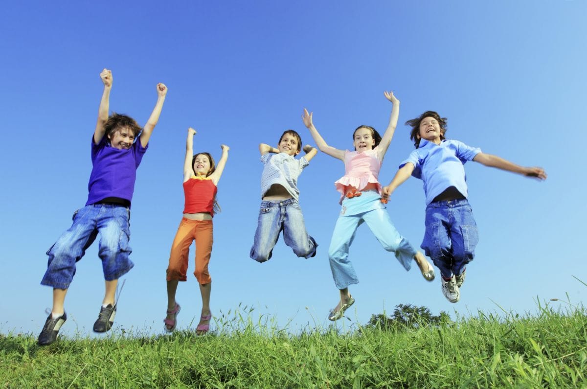 five kids jumping in the air in a grass field