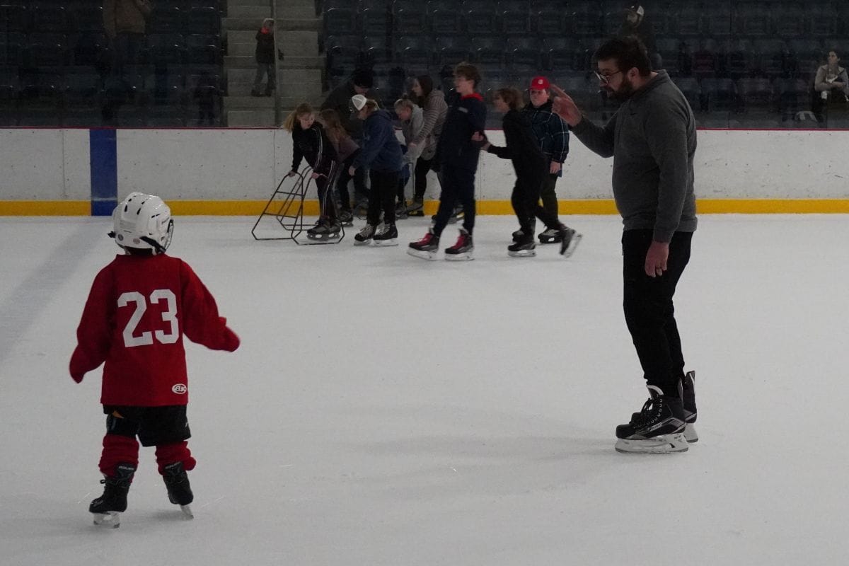 child in jersey on skates with adult and group of skates in background