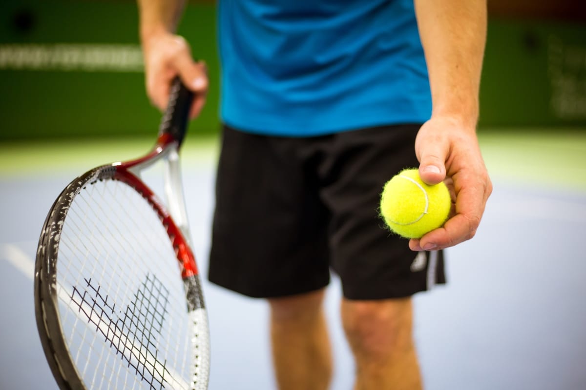 Close-up of man's hand holding tennis ball and racket