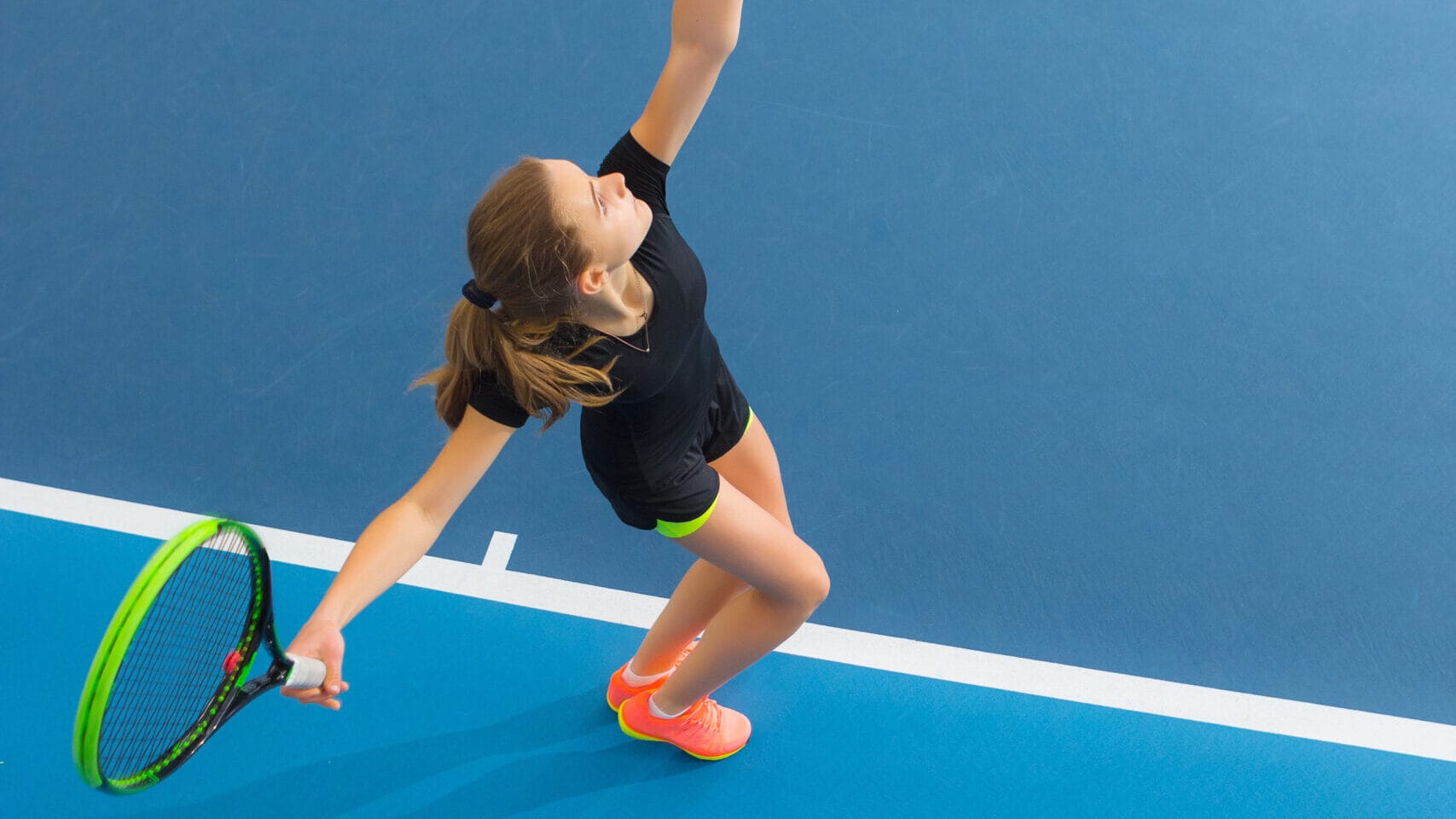 teenager prepares to hit tennis ball on a tennis court