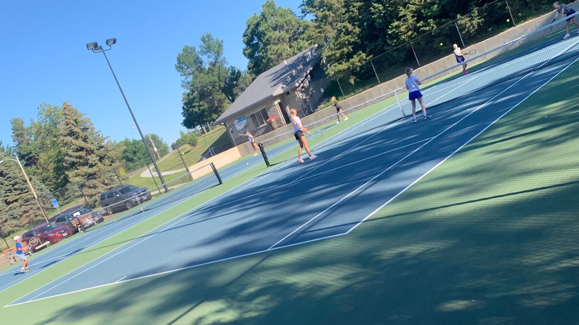 youth playing tennis on an outdoor court during the summer