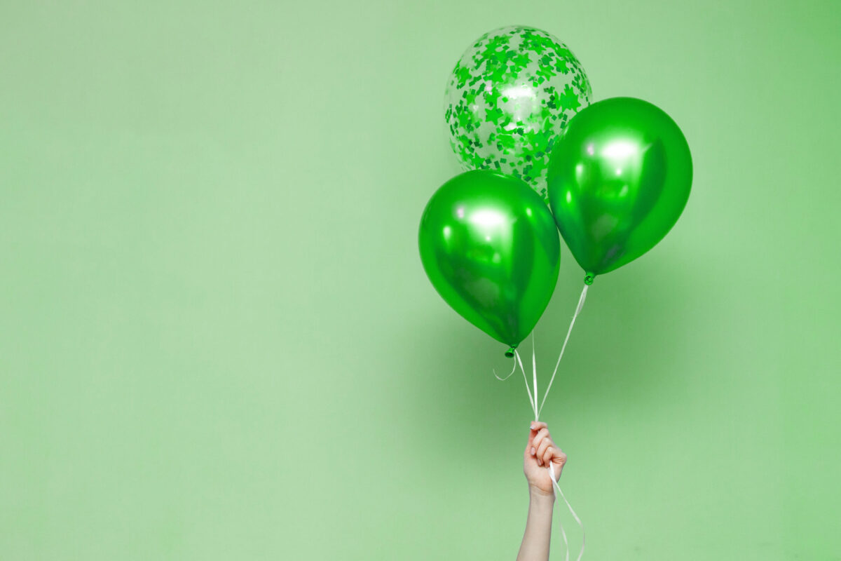 three green birthday balloons held up by someone's hand