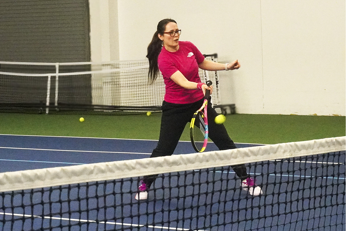 an adult hits a tennis ball near a net at an indoor tennis court