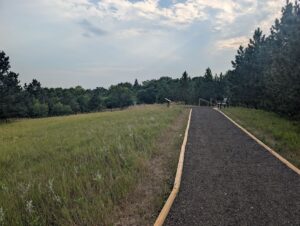 a trail with an interpretive sign and a park bench surrounded by prairie and trees at the arboretum