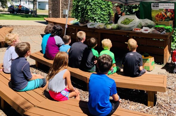 kids sitting on benches, learning about local produce